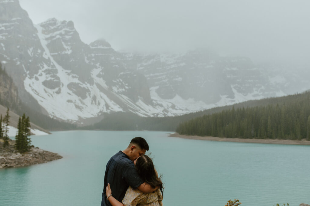 couple embracing in front of dramatic view of Moraine Lake, Canada