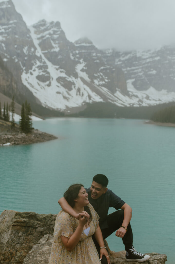 candid photos of couple laughing in the rain in front of Moraine Lake, Canada