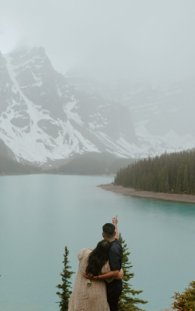 couple looking at view during rainy engagement session at Moraine Lake, Canada
