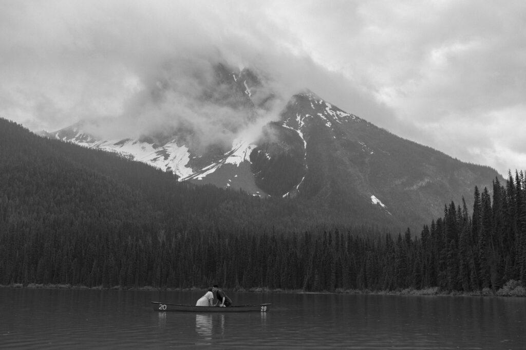 black and white landscape photo of couple kissing in a canoe in front of a dramatic mountain backdrop in Canada