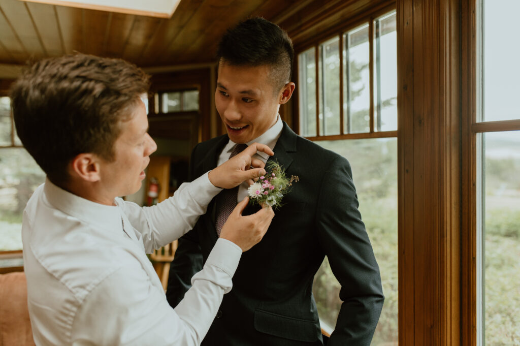 groom having boutonnière put on by friend before wedding ceremony in Alberta, Canada