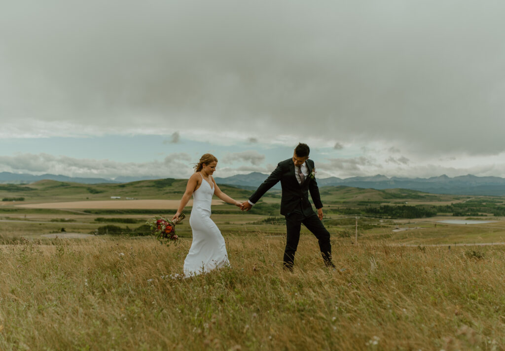couple walking through field in foothills of Alberta for wedding portraits